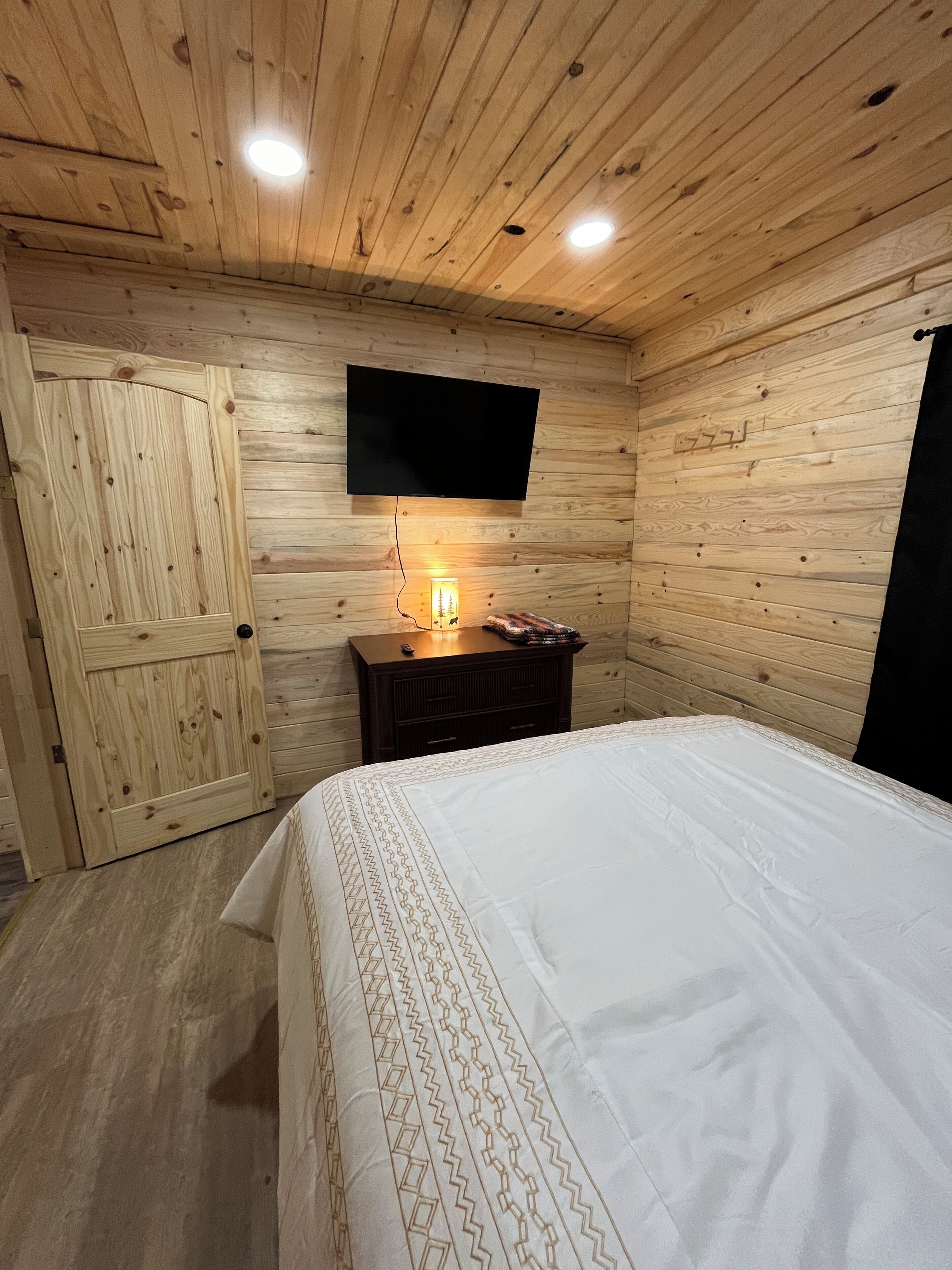Una stanza con rivestimenti in legno, un letto, una cassettiera, una televisione appesa al muro e una porta.