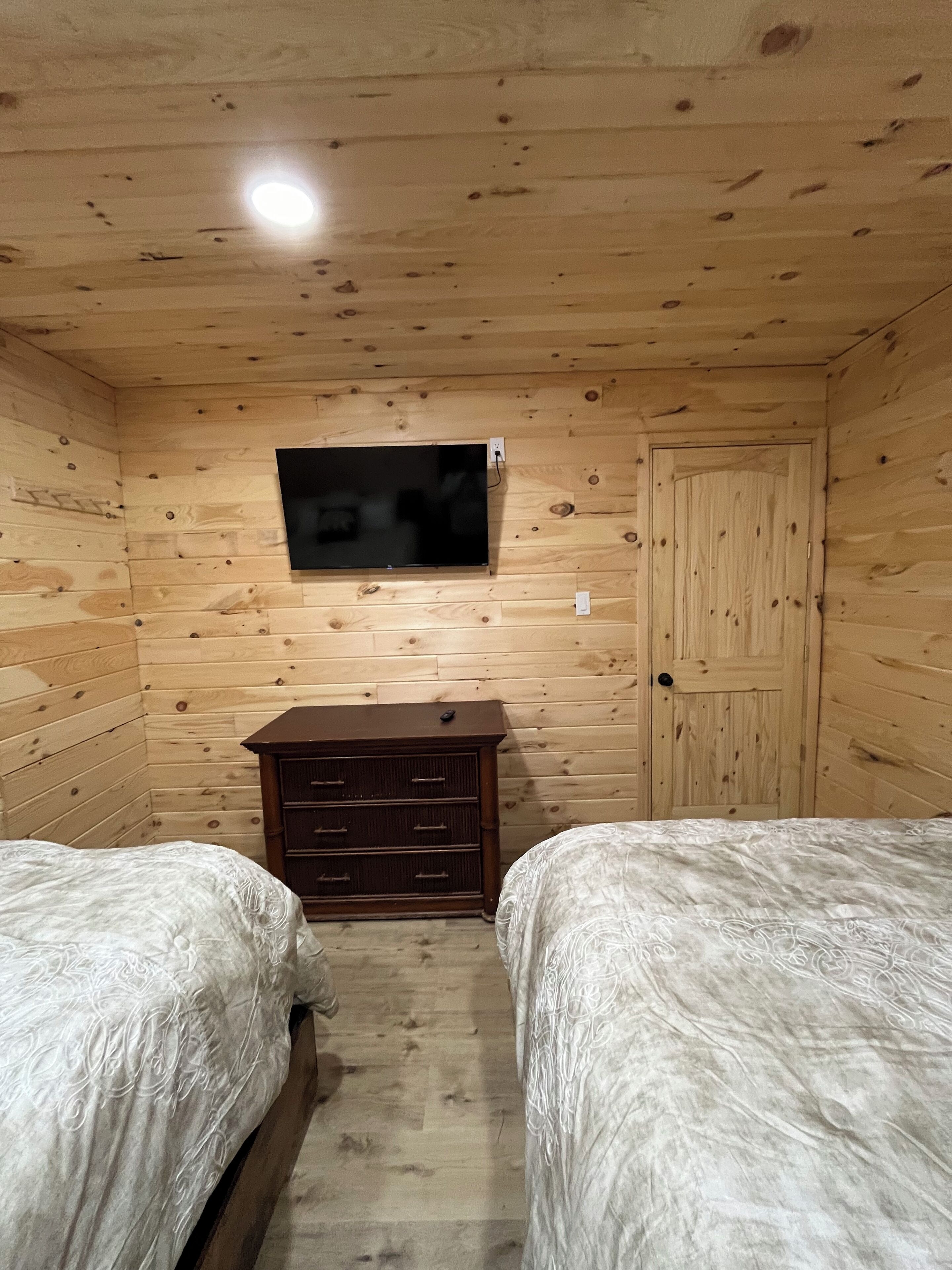 Una habitación pequeña y acogedora con paredes de madera, un televisor de pantalla plana montado en la pared, un aparador de madera y dos camas con ropa de cama estampada.