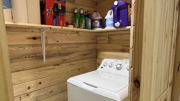 A compact laundry room with a washing machine, shelves with cleaning supplies, and a wooden wall design.