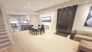 A modern living room with a fireplace, a dining area, and a kitchen in the background.