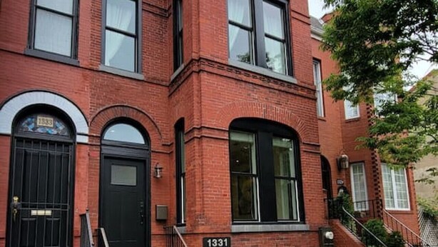 A red brick building with a black front door, a staircase leading to the entrance, and a number "1331" on the front.