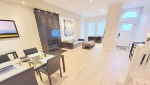 A modern living room with a glass dining table, dark chairs, a fireplace, a sofa, and a coffee table.