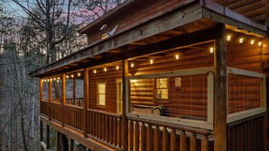 A wooden cabin with a balcony, multiple windows, and string lights.