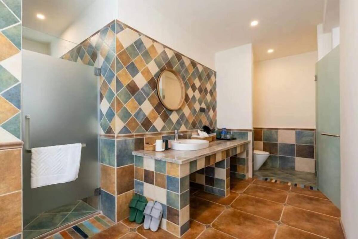A bathroom with a tiled backsplash, a sink, a mirror, and a shower area.