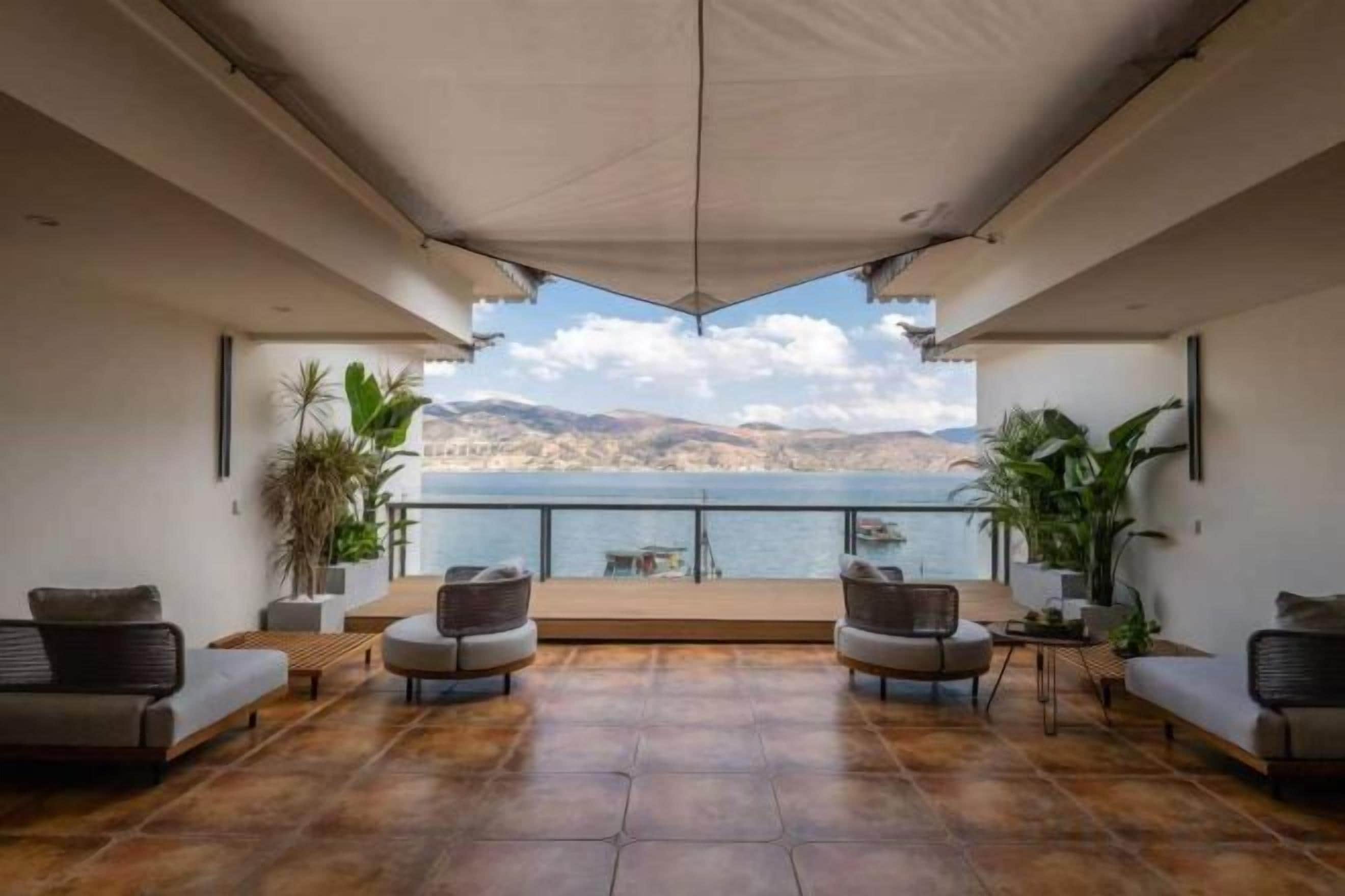 Una terraza con vista al mar, amueblada con sofás y sillones, y plantas en macetas.