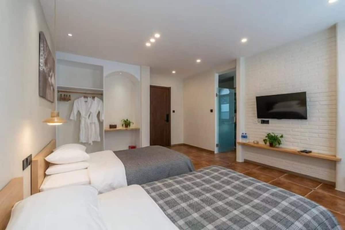 A hotel room with two beds, a TV mounted on the wall, a wardrobe, and a small shelf with toiletries.