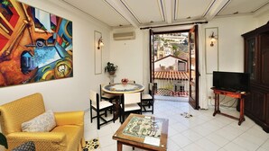 Een woonkamer met een gele bank, een ronde tafel, een tv op een standaard en een balkon met uitzicht op gebouwen.