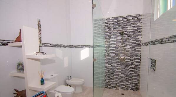 Un baño moderno con cabina de ducha de vidrio, sanitarios blancos y salpicadero de azulejos.