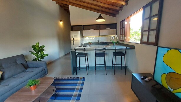 A modern kitchen with a central island, bar stools, and a grey sofa.