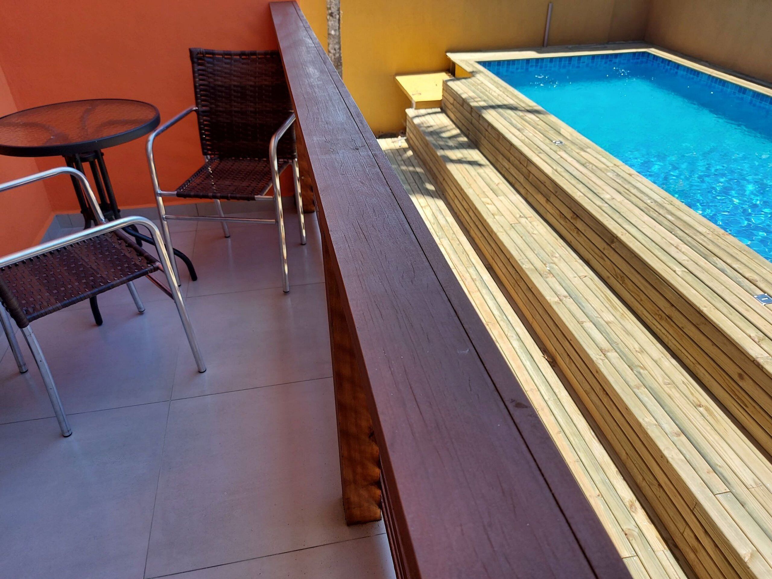 A poolside area with a wooden deck, a small round table, and two wicker chairs.
