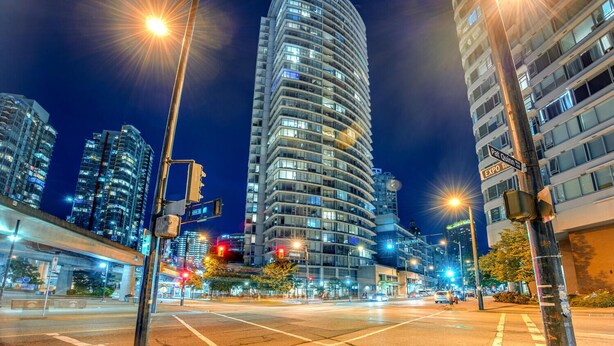 Ein nächtliches Stadtbild mit modernen Hochhäusern, Straßenlaternen und einem klaren Himmel.