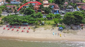 Eine Vogelperspektive zeigt einen Strand mit Reihen roter Liegestühle, einigen Sonnenschirmen und wenigen Personen.