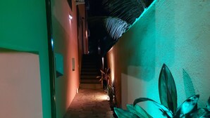 Passadís estret amb una escala que puja, una planta en testos a la dreta i una paret amb relleu a l'esquerra.