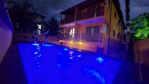 Una piscina amb il·luminació blava de nit, envoltada d'edificis.