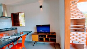 A compact living space with a kitchen, dining area, and a TV on a wooden stand. - Cedro - Cosy Flat Near the Beach with kitchen, private BBQ, pool (Paraty)