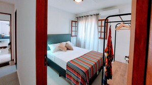 A bedroom with a bed, a wardrobe, a hanging rack, and a window with curtains. - Cedro - Cosy Flat Near the Beach with kitchen, private BBQ, pool (Paraty)