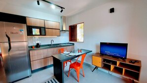 A modern kitchen with a refrigerator, microwave, and stove. There is a dining table with chairs and a television on a stand. - Cedro - Cosy Flat Near the Beach with kitchen, private BBQ, pool (Paraty)