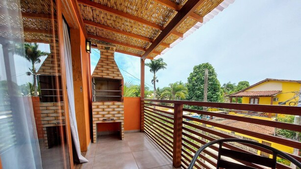 A balcony with a brick barbecue grill, a glass door, and a view of a yellow building. - Cedro - Cosy Flat Near the Beach with kitchen, private BBQ, pool (Paraty)