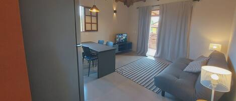 A modern living room with a sofa, a dining table with chairs, a ceiling fan, and a TV.