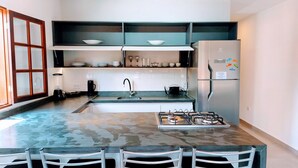 Una cucina compatta con piano cottura a gas, lavello e frigorifero. Ci sono pensili sopra il bancone e una finestra sulla sinistra.