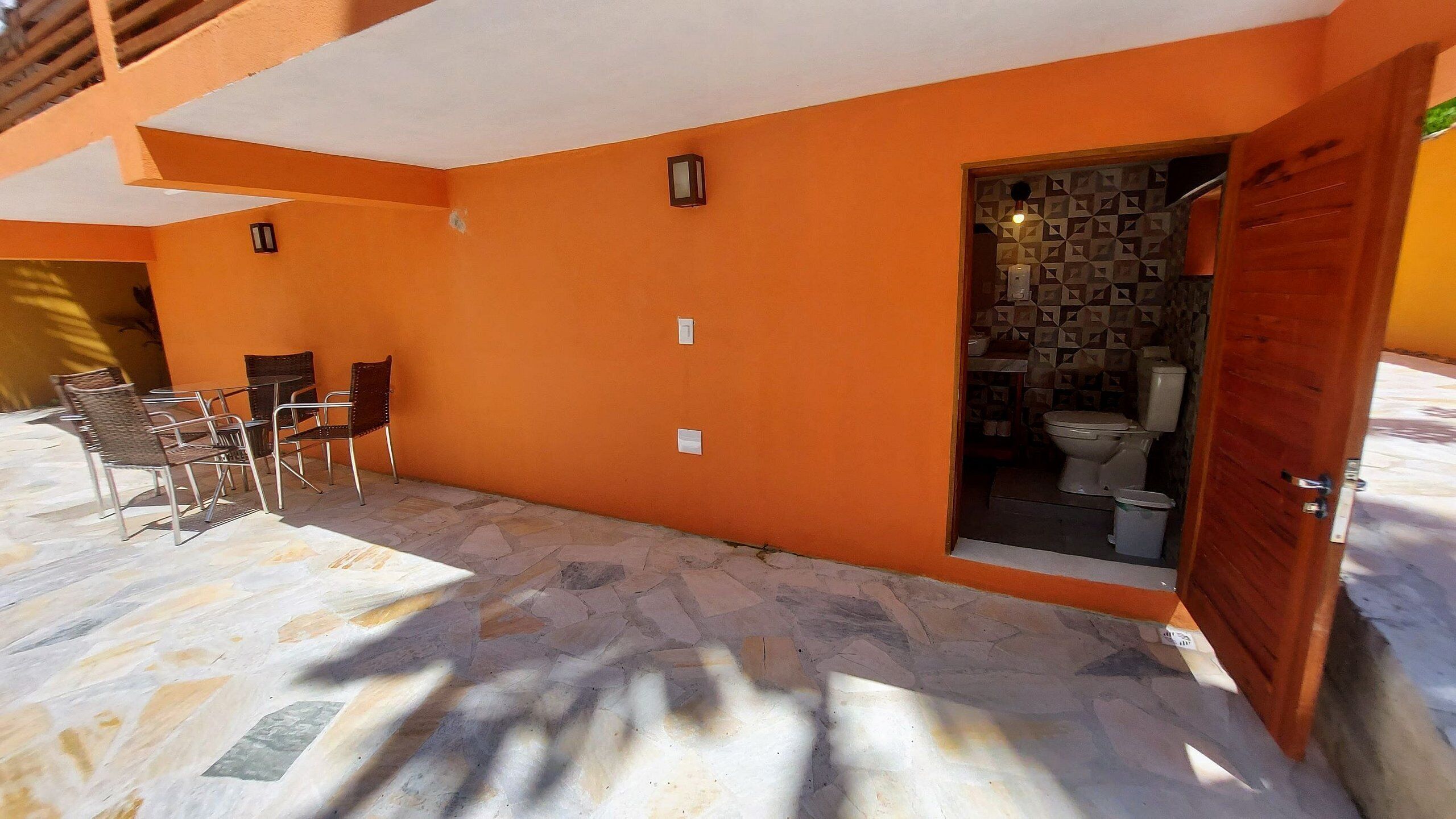 An outdoor patio with a table and chairs, a tiled floor, and a door leading to a bathroom with a toilet and sink.
