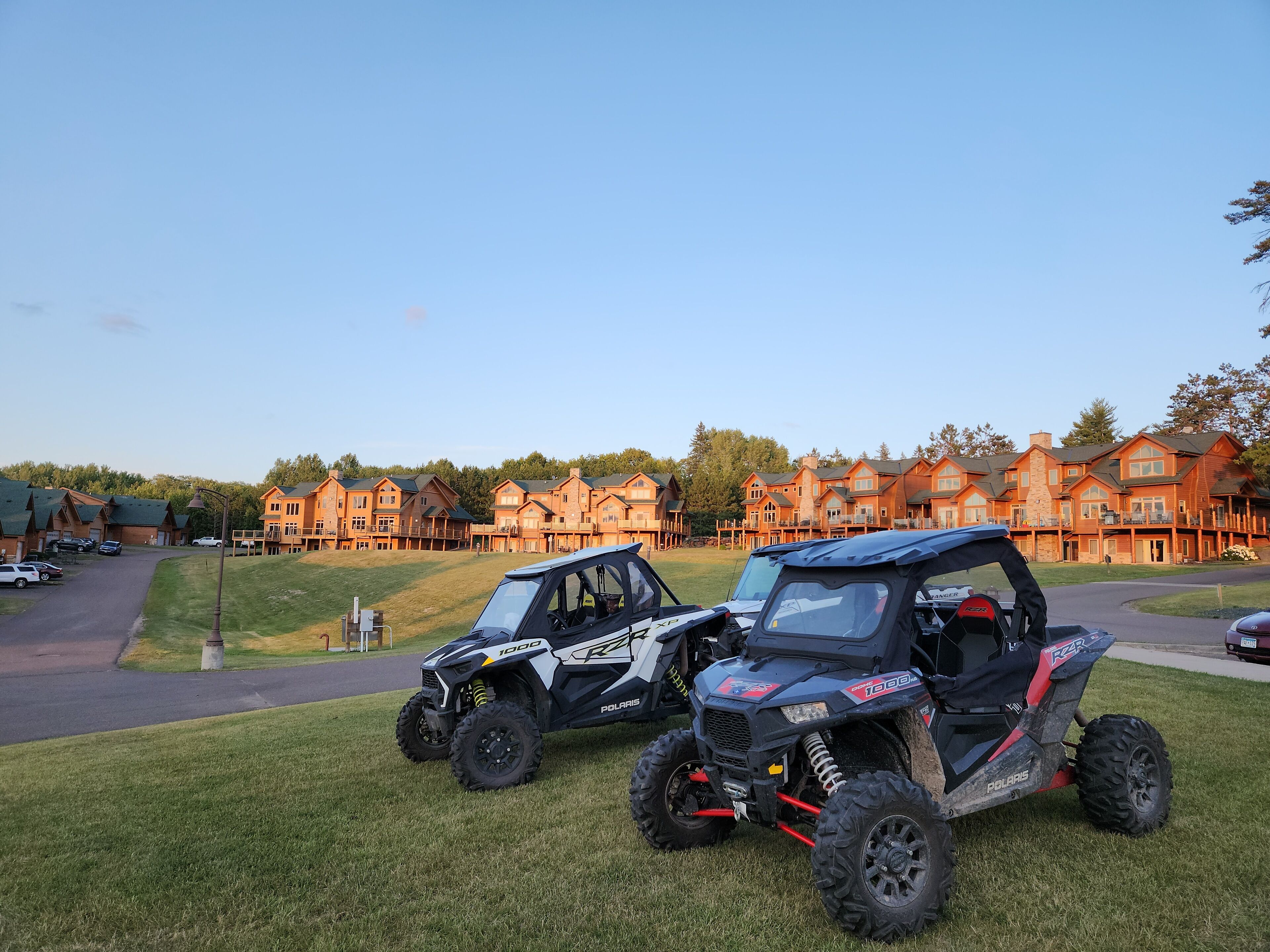 Two Polaris RZR vehicles parked on a grassy area with a large, multi-story building in the background.