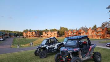 Two Polaris RZR vehicles parked on a grassy area with a large, multi-story building in the background.