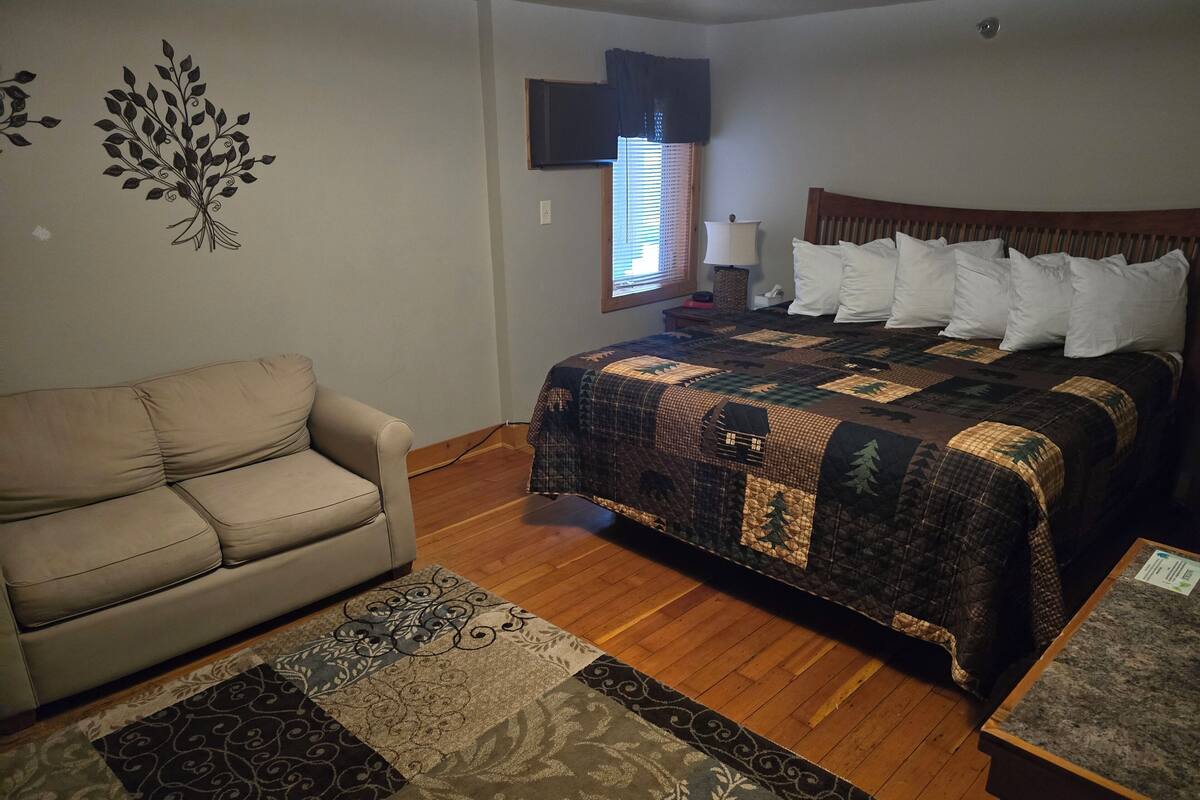 Un dormitorio con cama, sofá, ventana con persianas, lámpara y decoración en la pared.