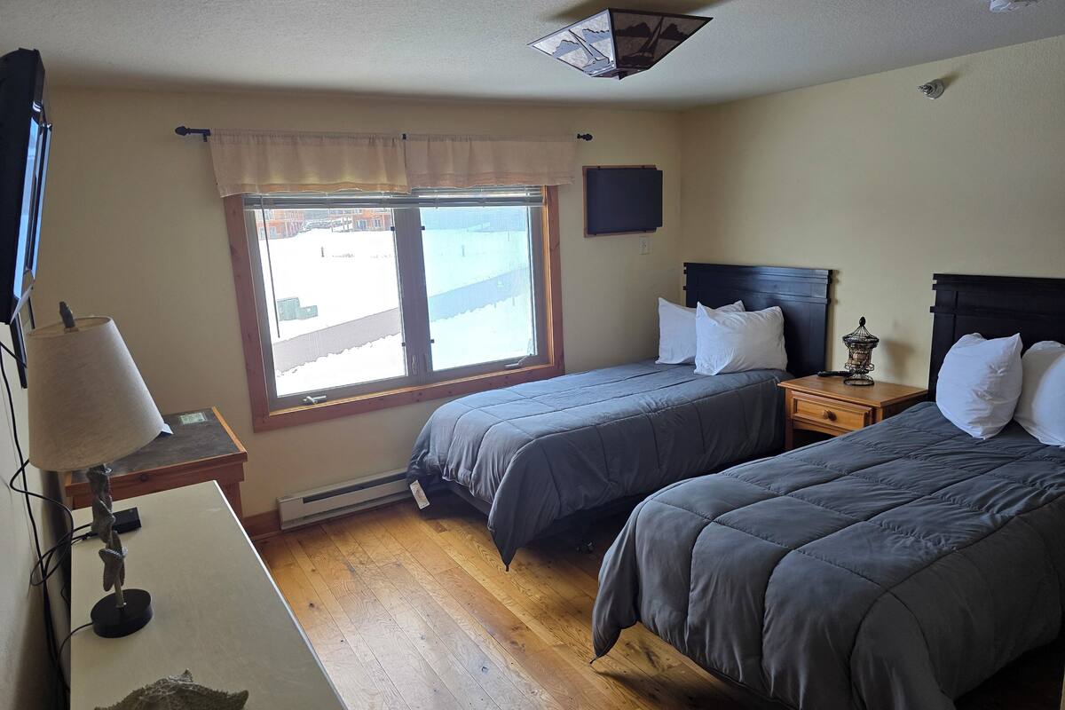 Un dormitorio con dos camas, una ventana con vistas, un ventilador de techo y una mesita de noche con una lámpara y un objeto decorativo.