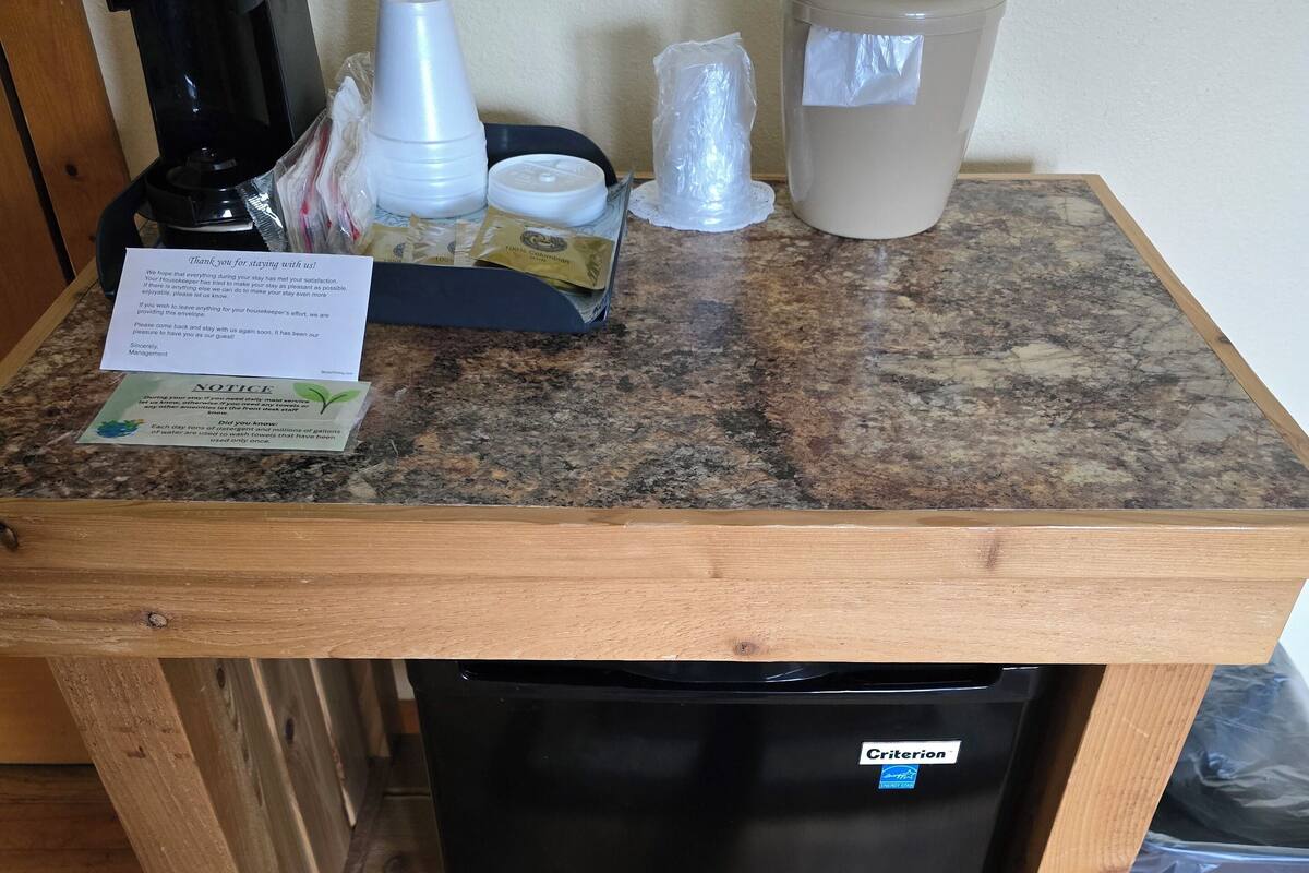 Una pequeña cocina con cafetera, basurero y refrigerador.