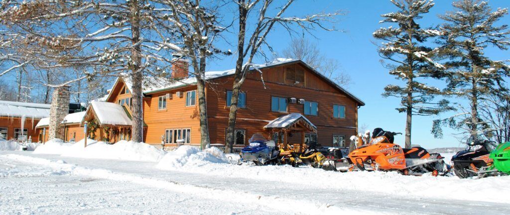 Un chalet en bois avec une allée enneigée et des motoneiges garées.