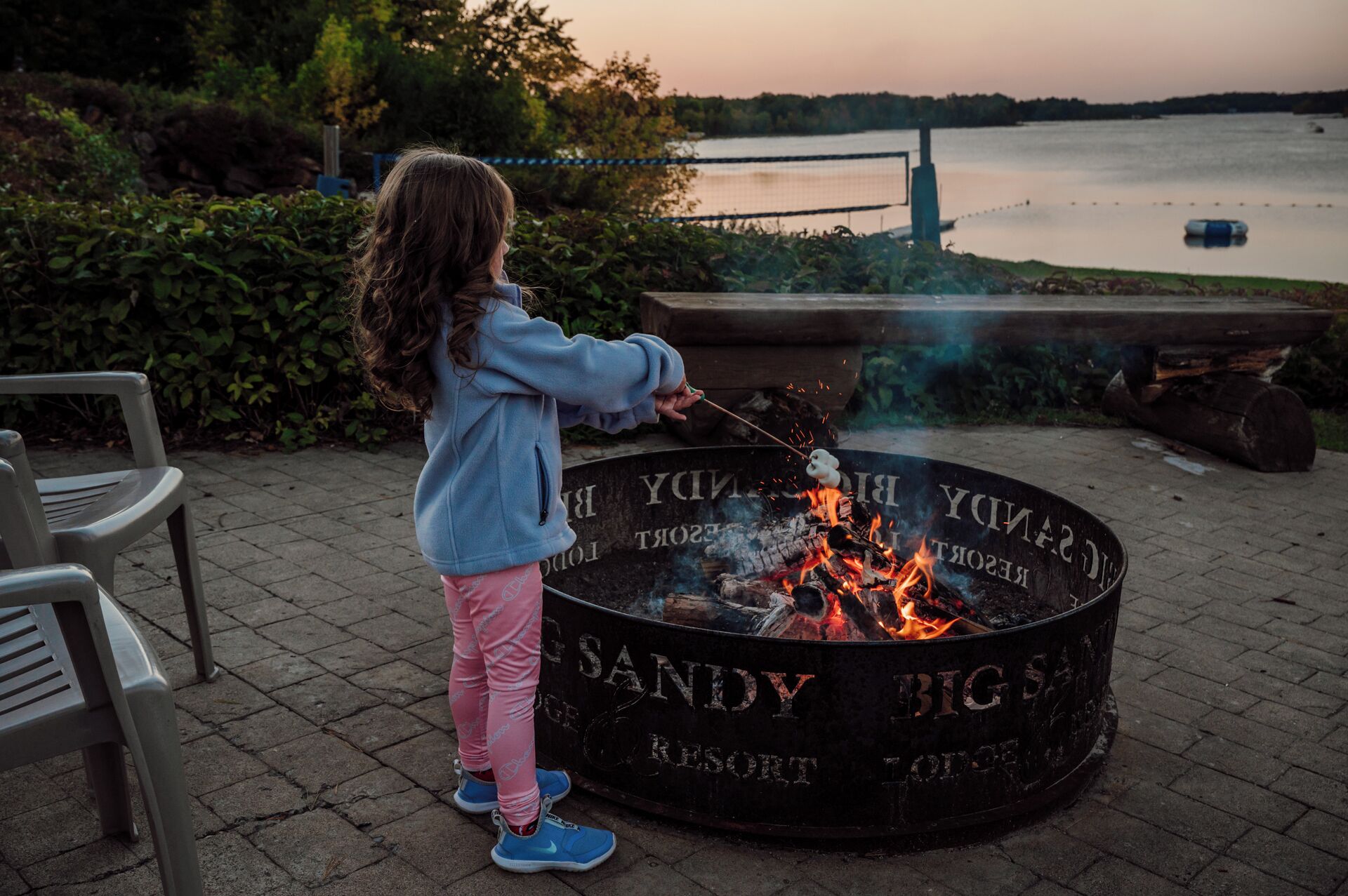 A child roasting marshmallows over a fire pit labeled "SANDY BIG SAN RESORT".