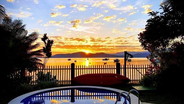 Una piscina con vistas a la puesta de sol, rodeada por una valla de madera y palmeras.