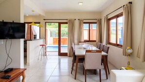A modern kitchen with a flat-screen TV, a dining area with a table and chairs, and a view of a swimming pool. - Safira House. Beautiful 3 suite house in front of the sea with private swimming pool and BBQ area (Paraty)