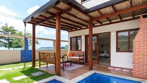 A covered patio with a pool, wooden furniture, and a view of the landscape. - Safira House. Beautiful 3 suite house in front of the sea with private swimming pool and BBQ area (Paraty)