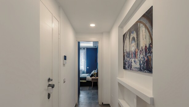 Un couloir avec un lit en arrière-plan, un tableau au mur et une porte sur la gauche.