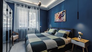 Une chambre à coucher moderne avec un grand lit, une table de chevet, une chaise et une fenêtre ornée de rideaux légers.