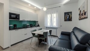 Une cuisine moderne avec des meubles blancs, un plan de travail noir et une table à manger avec des chaises. On y trouve également un canapé en cuir noir et un tableau accroché au mur.