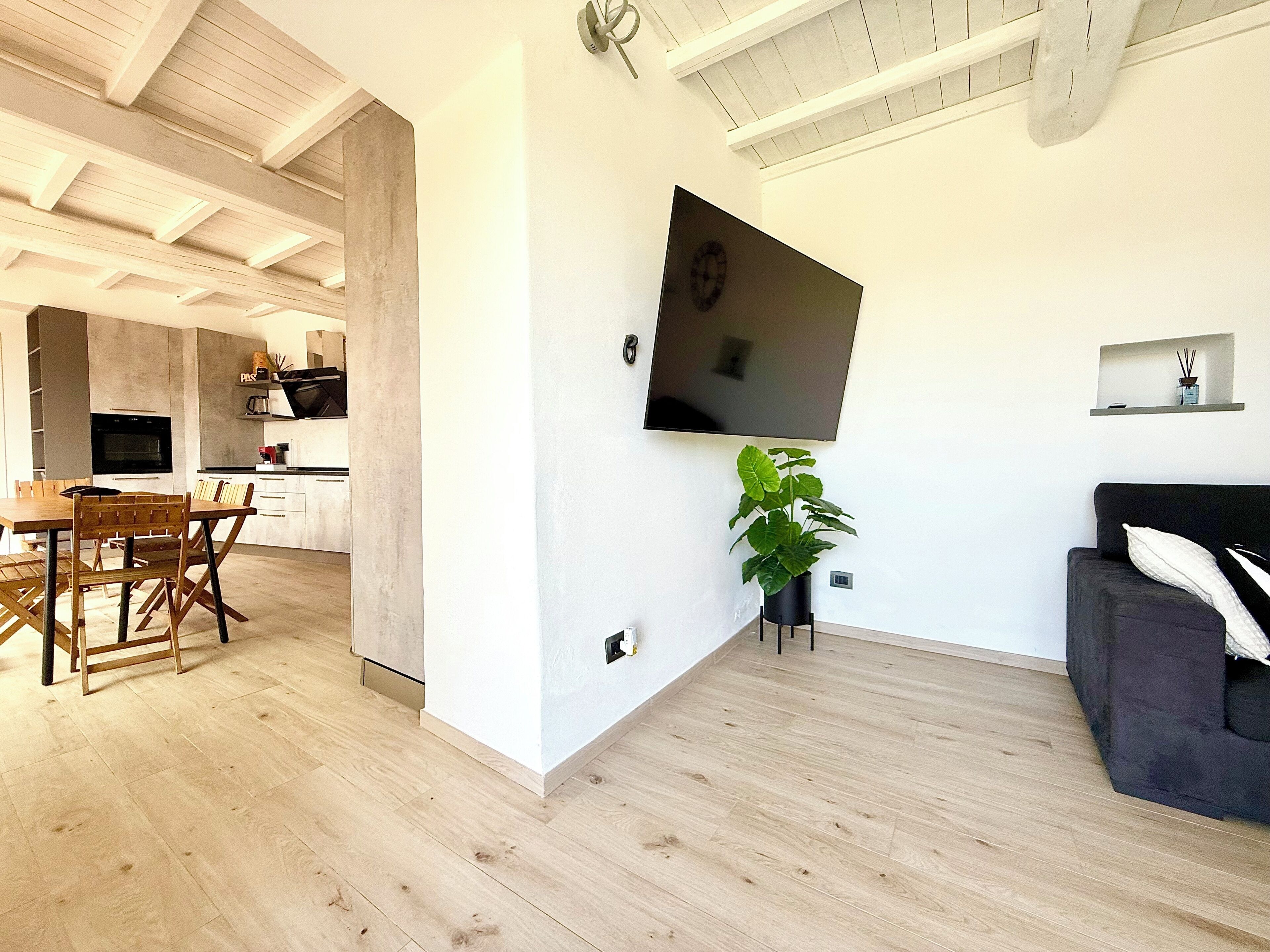 Ein modernes Wohnzimmer mit flachbildfernseher an der Wand, einem dunklen Sofa und einem Holzesstzimmer mit Stühlen.