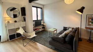 Una sala de estar moderna con un sofá, un sillón, un televisor, una estantería y una ventana.