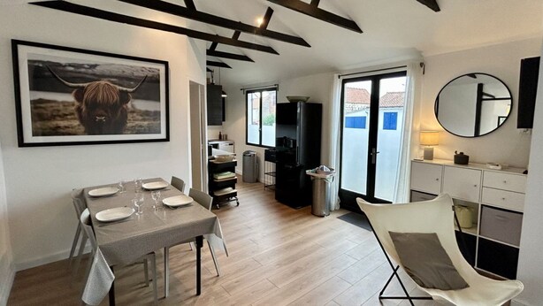 Un comedor con una mesa preparada para cuatro personas, una trona, un cuadro de una cabeza de toro montada y una zona de cocina con armarios y un refrigerador.