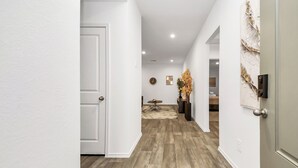 Un pasillo con suelo de madera, paredes blancas y una puerta a la izquierda.