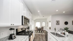Una cocina moderna con armarios blancos, encimera de granito, horno empotrado, microondas y un área de comedor con mesa y sillas.