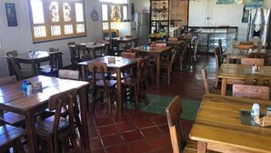 Un restaurante con mesas y sillas de madera, pisos con baldosas y una zona de cocina visible al fondo.