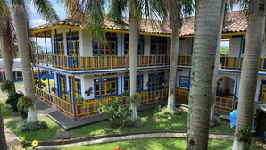 Un edificio de varios pisos con balcones, rodeado de palmeras y un jardín cuidado.