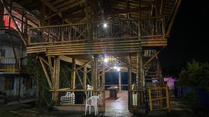 Una estructura de bambú con un pasillo cubierto y una silla blanca en el exterior.