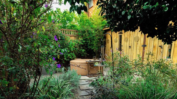 Un jardín con cerca de madera, un jacuzzi y un sendero de piedra.