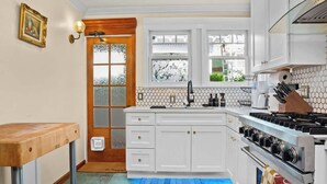 Una cocina con armarios blancos, estufa a gas y puerta de madera con paneles de vidrio.