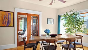 Un comedor con una mesa y sillas de madera, un ventilador de techo y un ventanal con vistas a zonas verdes.