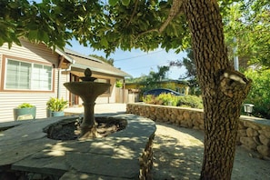Une fontaine en pierre dans un jardin, avec une maison en arrière-plan.